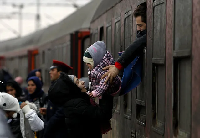 A refugee man passes a baby to a woman from a train window, upon their arrival at the transit center for refugees near northern Macedonian village of Tabanovce, Wednesday, February 10, 2016. Macedonian authorities are reinforcing a barrier at the country's border with Greece that is designed to limit the number of migrants and refugees crossing into the country, accepting people only from war-affected zones who declare Austria or Germany as their final destination. (Photo by Boris Grdanoski/AP Photo)