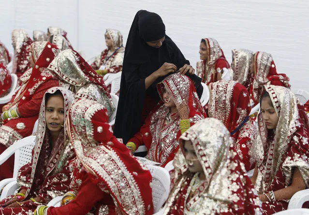 A Muslim bride is helped with her wedding dress, before the start of a mass marriage ceremony in Ahmedabad, India, February 7, 2016. (Photo by Amit Dave/Reuters)