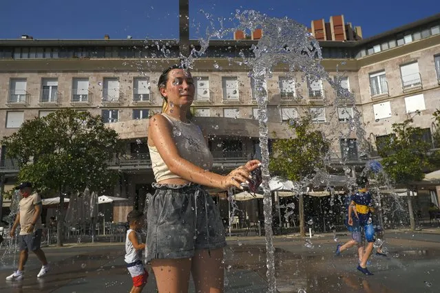 A woman cools off with the water to the fountain during a heatwave in Pamplona, northern Spain, Friday August 13, 2021. Stifling heat is gripping much of Spain and Southern Europe, and forecasters say worse is expected to come. (Photo by Alvaro Barrientos/AP Photo)