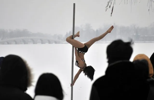 This picture taken on December 17, 2013 shows people watching a pole dancer practise after it snowed in Tianjin during a promotional event by members of China's national pole dancing team and students of the sport. (Photo by AFP Photo)