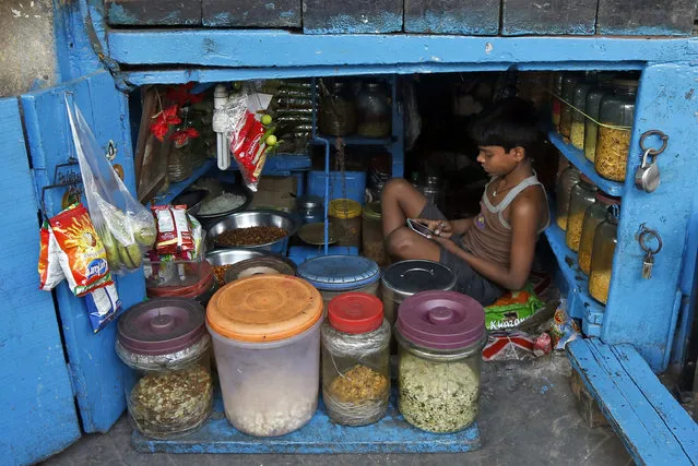 A boy uses a mobile phone as he sits inside his father's snacks shop along a road in Kolkata, India, February 22, 2016. (Photo by Rupak De Chowdhuri/Reuters)