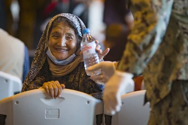A woman from Afghanistan smiles after being given a bottle of water after disembarking from a U.S. airforce plane at the Naval Station in Rota, southern Spain, Tuesday August 31, 2021. The United States completed its withdrawal from Afghanistan late Monday, ending America's longest war. (Photo by Marcos Moreno/AP Photo)