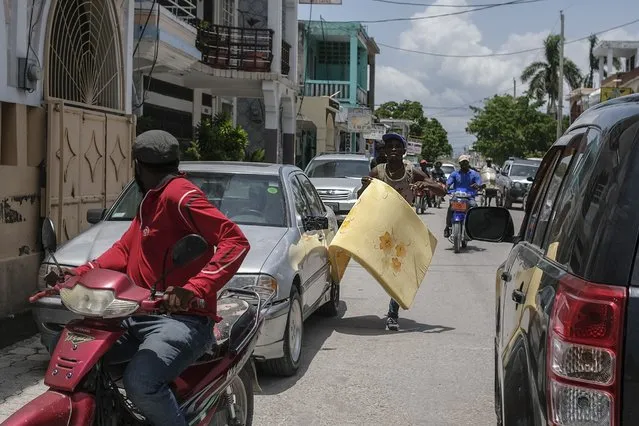 A man runs to get on a scooter and carry away a foam mattress after a group stole several of them from inside a Red Cross center in Les Cayes, Haiti, Friday, Aug. 20, 2021, six days after a 7.2 magnitude earthquake hit the area. (Photo by Matias Delacroix/AP Photo)
