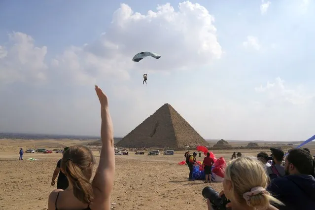 A parachutist is greeted by fans as he approachs the historical site of the Giza Pyramids, near Cairo, Egypt, Wednesday, November 2, 2022.  More than 100 parachutists from 16 countries are participating at “Jump Like a Pharaoh” festival at the site of Giza Pyramids ahead of COP27 to be held in Egypt in November 6. (Photo by Amr Nabil/AP Photo)