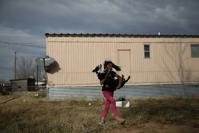 Rachel, daughter of Orfa, a migrant from Honduras, plays with the family's recently acquired dog Scott, outside the second trailer the family moved to in Texico, New Mexico, U.S., November 29, 2018. (Photo by Loren Elliott/Reuters)
