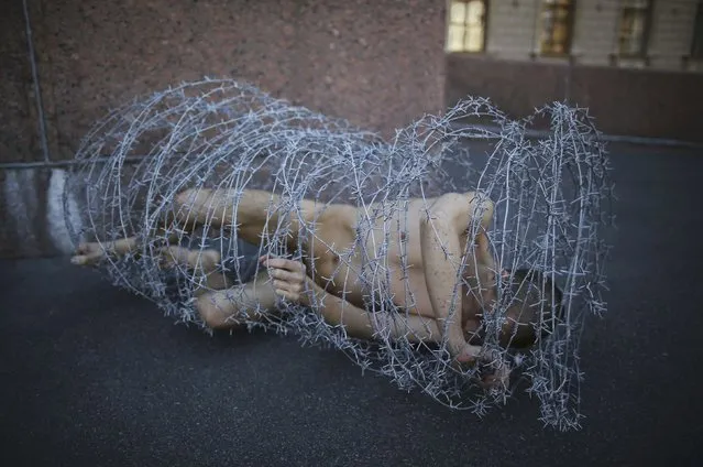 Artist Pyotr Pavlensky lies on the ground, wrapped in barbed wire roll, during a protest action in St. Petersburg, Russia, May 3, 2013. (Photo by Artur Bainozarov/Reuters)