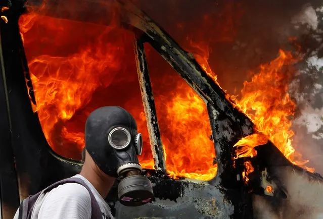 A protester wearing a gas mask walks beside a burning van during violent protests against austerity measures in Athens, Greece, June 28, 2011. (Photo by Yannis Behrakis/Reuters)