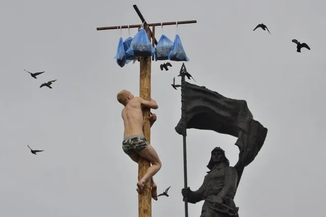 A man tries to climb a wooden pole to get a prize during Maslenitsa celebrations, with the Monument to Fighters for the Soviet Power in the Far East seen in the background, in the far eastern city of Vladivostok, Russia, March 13, 2016. Maslenitsa is widely viewed as a pagan holiday marking the end of winter and is celebrated with pancake eating, while the Orthodox Church considers it as the week of feasting before Lent. (Photo by Yuri Maltsev/Reuters)