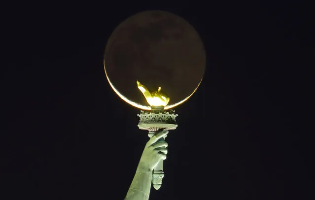 A 1.6 percent illuminated moon rises behind the torch on the Statue of Liberty before sunrise on November 3, 2021, as seen from Jersey City, New Jersey. (Photo by Gary Hershorn/Getty Images)