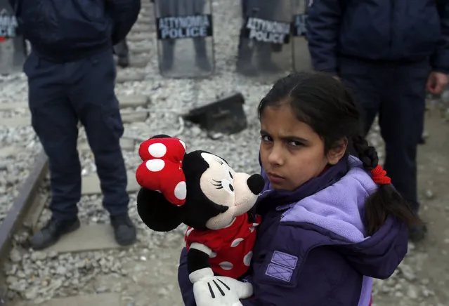 A migrant girl stands in from of Greek police cordon during a protest demanding the opening of the border between Greece and Macedonia in the northern Greek border station of Idomeni, Greece, Sunday, March 27, 2016. A split appears to have developed among the groups of migrants at the Idomeni border encampment, with Greek riot police who, so far, have used only their shields to protect the border. (Photo by Darko Vojinovic/AP Photo)
