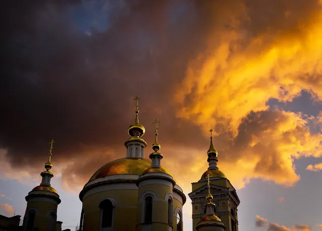 In this Tuesday, June 19, 2018 filer, clouds are illuminated by the sun setting sun over a church during the 2018 soccer World Cup in Podolsk near Moscow, Russia. (Photo by Michael Probst/AP Photo)