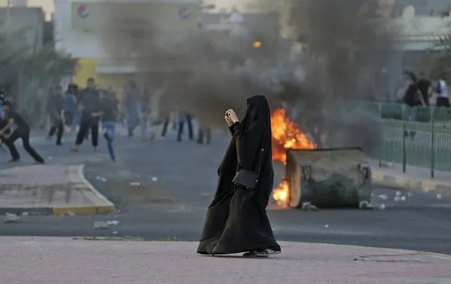 A Bahraini woman photographs approaching police as anti-government protesters clashed with riot police firing tear gas after the funeral of an 18-year-old in Shahrakan, Bahrain, on April 5, 2016. Thousands of Bahrainis marched in the politically charged funeral procession for Ali Abdulghani, who died of severe injuries sustained while fleeing arrest. (Photo by Hasan Jamali/AP Photo)