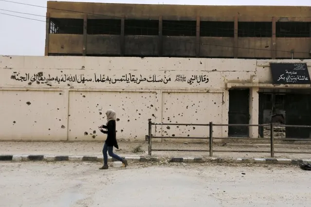 A woman walks near an Islamic State riddled school wall during her visit to the city of Palmyra, Syria April 9, 2016. The text on the sign (R) reads in Arabic: “Aisha, daughter of Abi Bakir school” and on the left is an islamic quote. (Photo by Omar Sanadiki/Reuters)