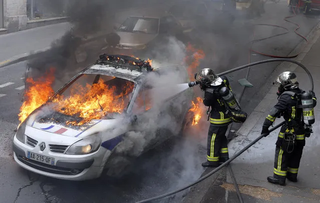 Firefighters work on a police car set up on fire by counter demonstrators while police forces gather to denounce the almost daily violent clashes at protests against a labor reform, Wednesday, May 18, 2016 in Paris. Several hundred counter demonstrators came chanting slogans like “everybody hates the police” and pushing up against officers until eventually the police deployed dispersal spray. (Photo by Francois Mori/AP Photo)