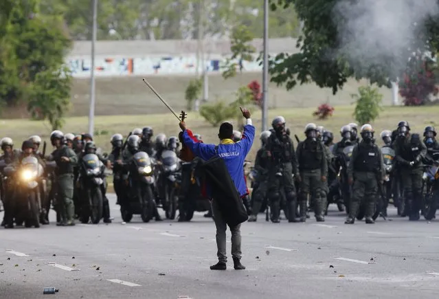 An anti-government protester raises his violin before National Guards, as he yells not to shoot at protesters, creating a brief pause during clashes in Caracas, Venezuela, Thursday, May 18, 2017. (Photo by Ariana Cubillos/AP Photo)