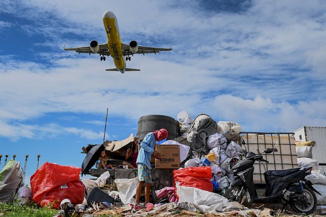 In this photo taken on December 27, 2023 a Cebu Pacific plane flies by as a man collects trash in Paranaque, Metro Manila. Inadequate garbage collection services, lack of disposal and recycling facilities, and grinding poverty have been blamed for the growing problem of plastic waste across the Philippines. (Photo by Jam Sta Rosa/AFP Photo)