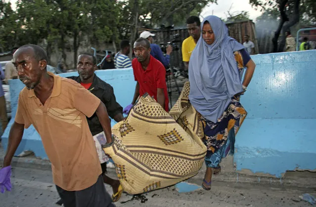 Somalis carry away the dead body of a person who was killed when a car bomb detonated in Mogadishu, Somalia, Wednesday, May 24, 2017. A Somali police officer says a number of people have been killed in a car bomb blast outside a restaurant near the port in the capital. (Photo by Farah Abdi Warsameh/AP Photo)