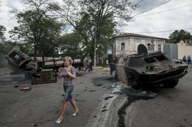 A local woman prepares to take pictures of a site of a battle  between Ukrainian troops and pro-Russian fighters in Mariupol, eastern Ukraine, Friday, June 13, 2014. Ukraine's interior minister says that government troops have attacked pro-Russian separatists in the southern port of Mariupol. Arsen Avakov said Friday that four government troops were wounded as forces retook buildings occupied by the rebels in the center of the town. (Photo by Evgeniy Maloletka/AP Photo)