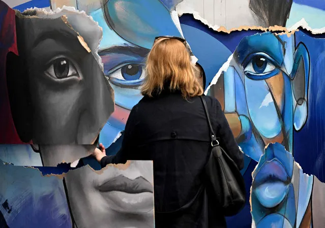 A vistor looks at a street art creation by French brothers artists Ensemble Reel on display during the second edition of “Le Colors Festival” in Paris on April 12, 2022. The ephemeral exhibition features some 90 artists over 700 square meters entirely dedicated to street art until May 8, 2022. (Photo by Emmanuel Dunand/AFP Photo)