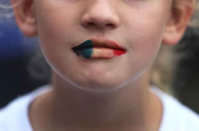A young woman paints her lips in the gay pride colors as she attends a one year anniversary memorial service for victims of the mass shooting at the Pulse gay nightclub being held at Lake Eola Park on June 12, 2017 in Orlando, Florida. Omar Mateen killed 49 people at the club a little after 2 a.m. on June 12, 2016. (Photo by Joe Raedle/Getty Images)