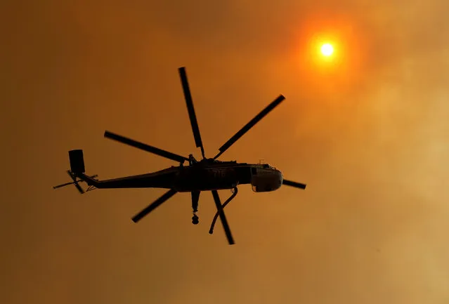 A fire fighting helicopter  passes through smoke under the sun as it helps battle a wildfire near Potrero California, U.S. June 20, 2016. (Photo by Mike Blake/Reuters)