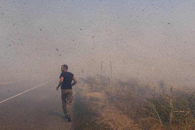 A Ukrainian serviceman runs to help farmers extinguish a burning field near Pokrovsk, Donetsk region, on September 16, 2024, amid the Russian invasion of Ukraine. (Photo by Oleksii Filippov/AFP Photo)