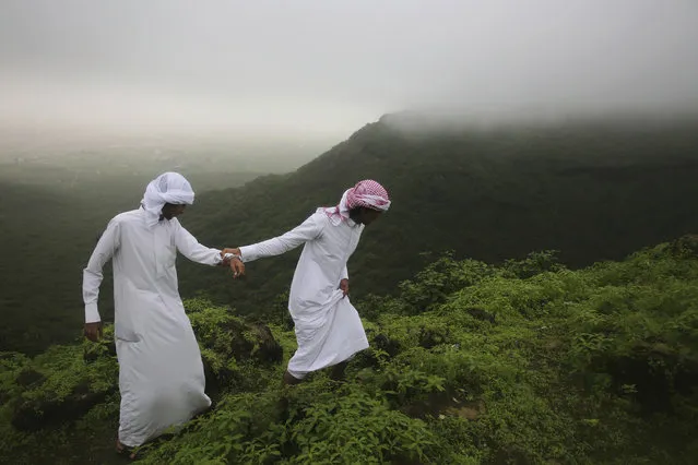 Mohammad al-Bariki, right, 17, leads his half-brother Sagheer al-Bariki, 17, across a cliff ledge in the fog-covered Jabal Ayoub mountains north of Salalah in southern Oman during the annual summer monsoon on Wed. August 2, 2017. The otherwise extremely arid region blooms when the monsoon, known as "al-khareef" in Arabic, drenches the southern Arabian peninsula with rainy clouds and drives stormy seas as locals and tourists celebrate the rain. While temperatures soar across the Arabian Peninsula, the cooler monsoon fog draws tens of thousands of tourists every summer. (Photo by Sam McNeil/AP Photo)