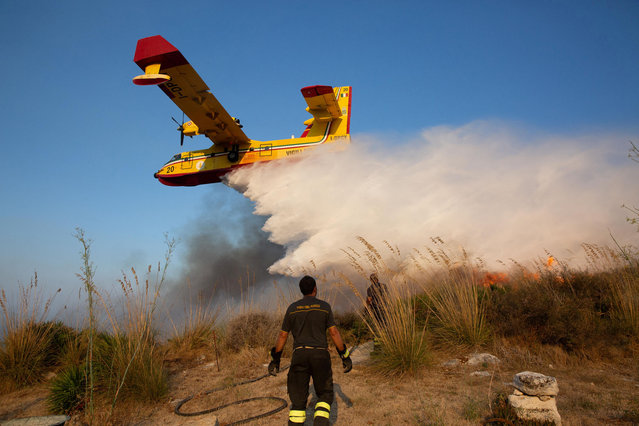 A fireman looks on as a Canadair aircraft drops water to extinguish a wildfire in Sicily's Trapani, Italy on August 27, 2023. (Photo by Antonio Cascio/Reuters)