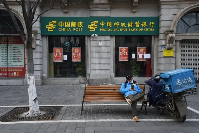 A delivery worker checks his mobile phone outside a Postal Savings Bank of China branch in Wuhan, February 25, 2020. (Photo by Reuters/China Stringer Network)