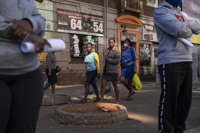 Three women carrying grocery bags walk past residents lining up to be tested for COVID-19 as well as HIV and Tuberculosis, in downtown Johannesburg Thursday, April 30, 2020. (Photo by Jerome Delay/AP Photo)