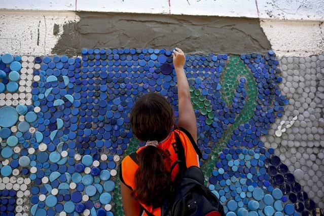 A woman sticks plastic bottle caps onto cement in a section of a 270-square-meter mural that Venezuelan artist Oscar Olivares is making with the help of residents in a bid to make the mural bigger of the world in Guatire, state of Miranda. Venezuela, on August 21, 2022. (Photo by Pedro Rances Mattey/Anadolu Agency via Getty Images)