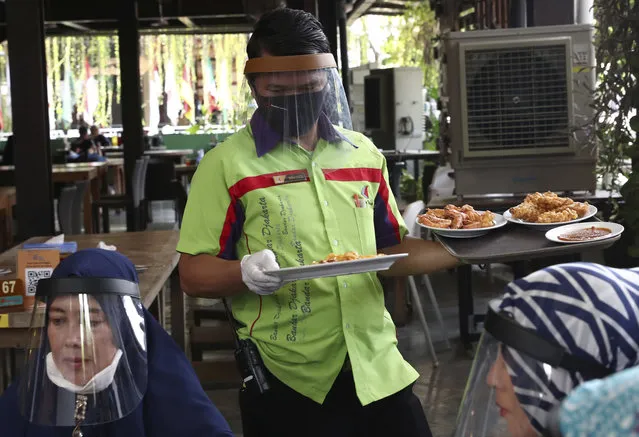 A waiter wearing protective face shield to help curb the spread of the new coronavirus delivers dishes to customers at a seafood restaurant on the outskirts of Jakarta, Indonesia, Wednesday, June 10, 2020. As Indonesia's overall virus caseload continues to rise, Jakarta has moved to restore normalcy by lifting some restrictions this week, saying that the spread of the virus in the city of 11 million has slowed after peaking in mid-April. (Photo by Tatan Syuflana/AP Photo)