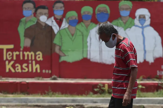 A man wearing a face mask walks past a coronavirus-themed mural in Jakarta, Indonesia, Thursday, October 1, 2020. (Photo by Achmad Ibrahim/AP Photo)