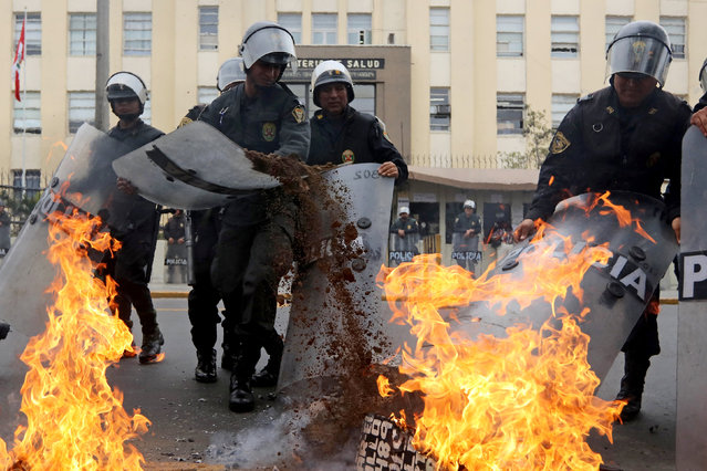 Riot police officers try to put out a burning cross before removing it during a protest against the government outside the Ministry of Health to demand better working conditions, in Lima, September 28, 2016. (Photo by Guadalupe Pardo/Reuters)