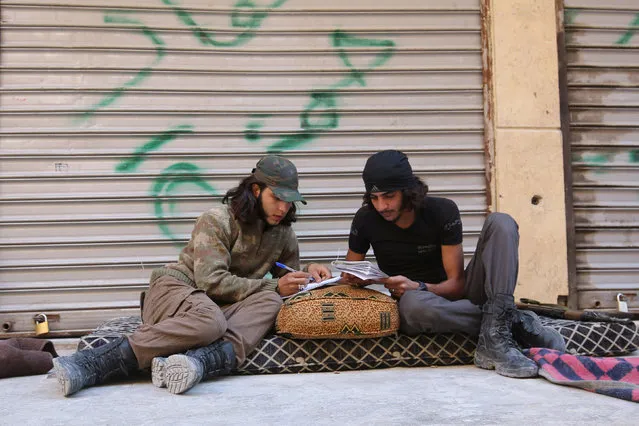 A Free Syrian Army fighter writes on a notebook as he sits with his fellow fighter in the rebel-held al-Myassar neighbourhood of Aleppo, Syria, September 27, 2016. (Photo by Abdalrhman Ismail/Reuters)