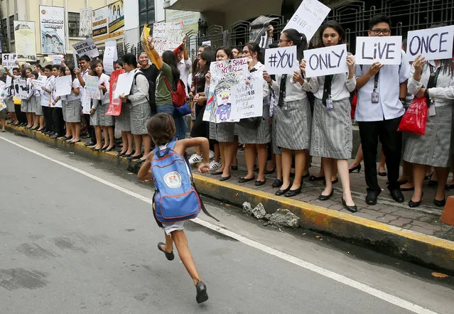 A school girl runs in front of students from St. Paul's University, a Roman Catholic school, as they come out from their campus to protest the killings being perpetrated in the unrelenting “War on Drugs” campaign of President Rodrigo Duterte, Friday, September 30, 2016 in Manila, Philippines. Duterte raised the rhetoric over his bloody anti-crime war to a new level Friday, comparing it to Hitler and the Holocaust and saying he would be “happy to slaughter” 3 million addicts. Duterte issued his latest threat against drug dealers and users early Friday on returning to his hometown in southern Davao city after visiting Vietnam, where he discussed his anti-drug campaign with Vietnamese leaders and compared notes on battling the problem. (Photo by Bullit Marquez/AP Photo)