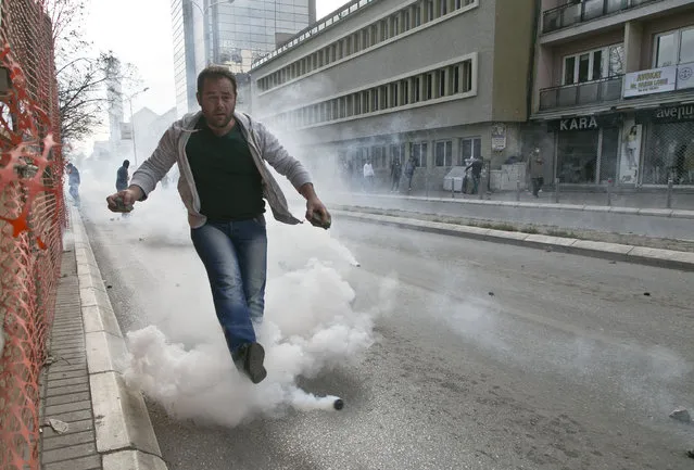 Supporter of the opposition throws back a tear gas canister at police forces in Kosovo capital Pristina on Wednesday, November 18, 2015, as scores of opposition supporters gathered in front of the government headquarters in downtown Pristina, throwing stones and paint against the building. (Photo by Visar Kryeziu/AP Photo)