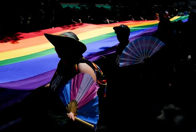 Mac Weatherill, left, and Yexara Colón Martinez, second from left, hold transgender pride fans as they help carry a large rainbow flag on their fourth anniversary during the annual Seattle Pride Parade, Sunday, June 25, 2023, in Seattle. (Photo by Lindsey Wasson/AP Photo)