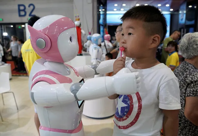 A boy stands next to an iPal robot at Avatarmind's booth at the World Robot Conference (WRC) in Beijing, China on August 17, 2018. (Photo by Jason Lee/Reuters)