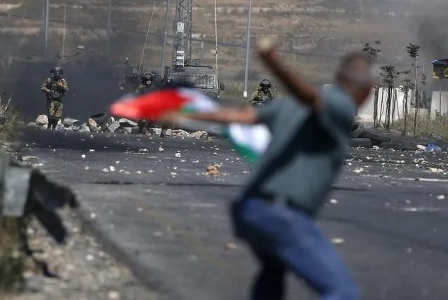A Palestinian demonstrator hurls a rock towards Israeli forces during clashes near the Jewish settlement of Beit El near Ramallah in the occupied West Bank on May 14, 2021. Israel faced a widening conflict, as deadly violence escalated across the West Bank amid a massive aerial bombardment in Gaza and unprecedented unrest among Arabs and Jews inside the country. The West Bank clashes, described as among the most intense since the second intifada that began in 2000, left seven people dead from Israeli fire, the Palestinian health ministry said, as the death toll from strikes in Gaza rose to 122. (Photo by Abbas Momani/AFP Photo)