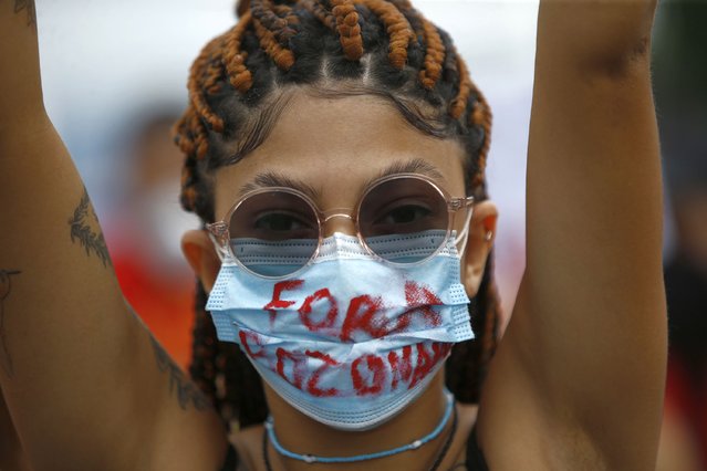 A woman wearing a protective face mask marked with a message that reads in Portuguese: “Get Out Bolsonaro” during a protest against Brazilian President Jair Bolsonaro's handling of the coronavirus pandemic and economic policies they say harm the interests of the poor and working class, in Rio de Janeiro, Brazil, Saturday, June 19, 2021. Brazil is approaching an official COVID-19 death toll of 500,000 – second-highest in the world. (Photo by Bruna Prado/AP Photo)