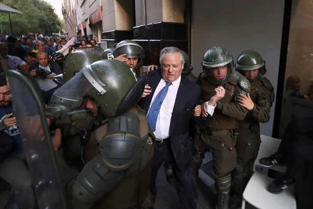 Ivan Arostica, president of the Constitutional Court, is escorted by riot policemen as demonstrators protest against an appeal from government coalition Chile Vamos to nullify a draft law that further restricts human rights abusers from getting prison benefits, according to local media, in Santiago, Chile December 19, 2018. (Photo by Ivan Alvarado/Reuters)