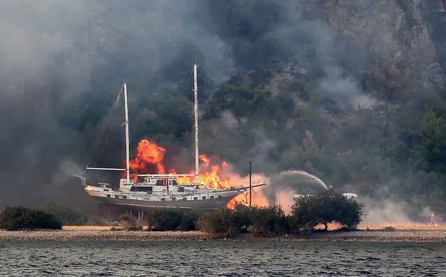 Firefighters battle to extinguish flames netx to a boat during the wildfires at the Milas district of Mugla, Turkey, 02 August 2021. At least eight people have died in the wildfires raging in Turkey's Mediterranean towns, the Turkish health ministry confirmed on 02 August 2021. (Photo by Erdem Sahin/EPA/EFE)