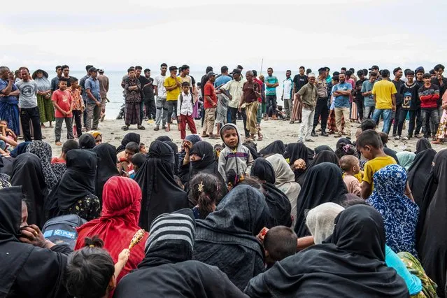 Rohingya refugees sit together on the ground after they arrived by boat at the Kalee beach in Laweung in Indonesia's Aceh province on November 14, 2023. Nearly 200 Rohingya refugees, including many women and children, landed in Indonesia's westernmost province on November 14, a local official said, the largest contingent of the persecuted Myanmar minority to arrive in months. (Photo by Jon S/AFP Photo)
