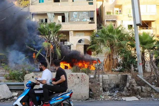 Lebanese men ride a motorcycle past a vehicle following clashes in the Khalde area, south of the capital, on August 1, 2021. At least five people including three Hezbollah members were killed south of Beirut when a funeral procession for a party member was ambushed, a Lebanese security source told AFP, adding that several people were wounded in the exchange of fire in the Khalde area between members of the Lebanese Shiite group and Sunni residents. (Photo by Anwar Amro/AFP Photo)