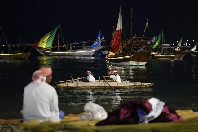 Fishermen ride a small boat as pearl boats don the flags of teams participating in the World Cup at Katara Beach during soccer tournament, in Doha, Qatar, Thursday, November 24, 2022. (Photo by Julio Cortez/AP Photo)