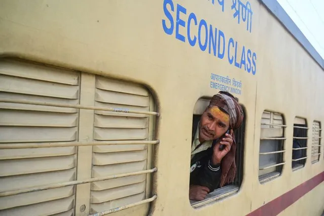 A farmer speaks on a mobile phone as he looks out from an overcrowded train as he returns home after taking a holy dip at Sangam, the confluence of rivers Ganga, Yamuna and mythical Saraswati, for the annual Hindu religious festival “Magh Mela” in Prayagraj on January 18, 2024. (Photo by Sanjay Kanojia/AFP Photo)