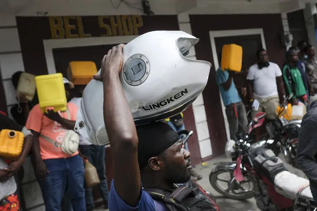 A man balances his motorbike tank on his head as he waits outside a gas station in hopes of filling his tank, in Port-au-Prince, Haiti, Saturday, October 23, 2021. The ongoing fuel shortage has worsened, with demonstrators blocking roads and burning tires in Haiti's capital to decry the severe shortage and a spike in insecurity. (Photo by Matias Delacroix/AP Photo)