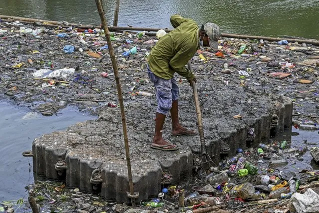 A worker removes garbage to clean a lake on the outskirts of Colombo on October 11, 2021. (Photo by Ishara S. Kodikara/AFP Photo)
