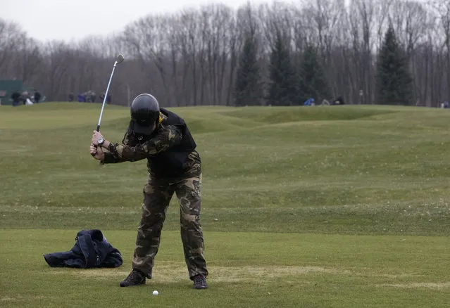 A man plays golf as anti-government protesters walk on the grounds of the Mezhyhirya residence of Ukraine's President Viktor Yanukovich in the village Novi Petrivtsi, outside Kiev February 22, 2014. (Photo by Konstantin Chernichkin/Reuters)